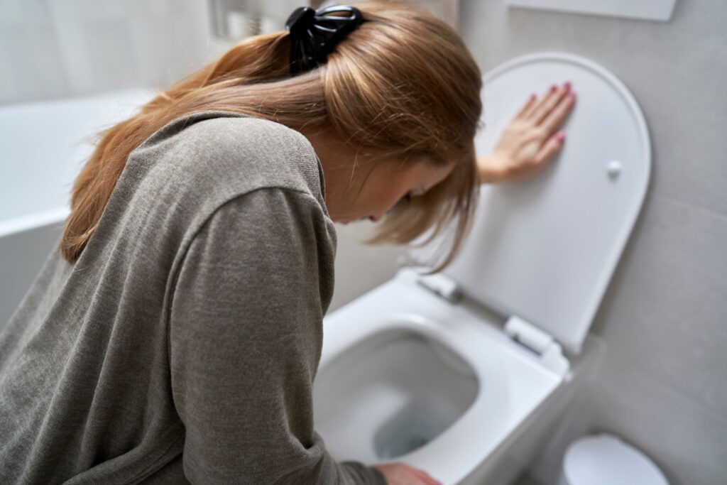 Mujer con malestar en el baño, apoyada en el inodoro. Experimentando una migraña.