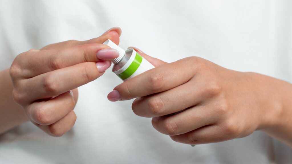 Manos abriendo un tubo de crema tópica para el tratamiento de las verrugas vaginales.