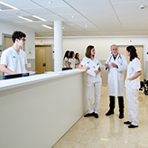 Estancias formativas. Estudiantes y profesional médico hablando en un pasillo de hospital.