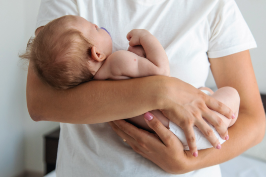 Madre con camiseta blanca sosteniendo con ternura en sus brazos a un bebé recién nacido con chupete