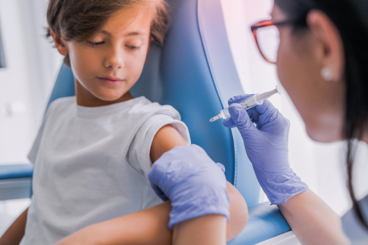 Médico pediatra aplicando una vacuna en el brazo de un niño en la consulta.