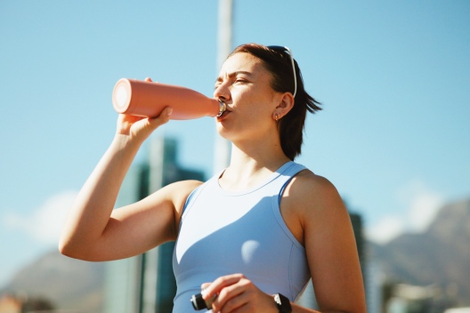 Mujer deportista bebiendo agua de una botella rosa al aire libre para mantener la hidratación al correr.