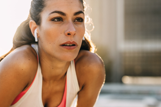 Primer plano de una corredora con auriculares inalámbricos, mostrando una expresión de concentración y determinación mental durante su entrenamiento.