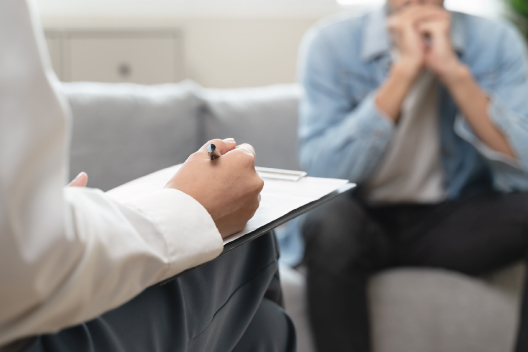 Psicólogo tomando notas en portapapeles durante una consulta con un paciente con estrés postvacacional.
