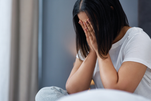 Mujer sentada cubriéndose el rostro con las manos en un gesto de angustia emocional y depresión.