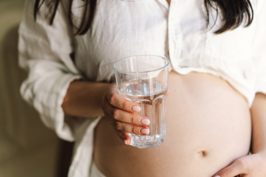 Mujer embarazada sosteniendo un vaso de agua para mantenerse hidratada y prevenir la deshidratación por hiperémesis gravídica.