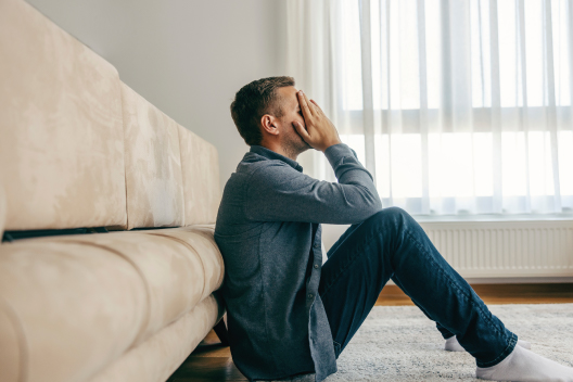 Hombre sentado en el suelo cubriéndose el rostro con angustia, reflejando los síntomas emocionales y la ansiedad por TOC.