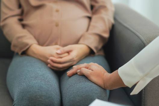 Mano de un especialista en salud ofreciendo apoyo y consuelo a una mujer embarazada sentada en un sofá durante una consulta médica