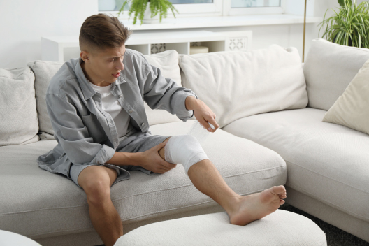 Joven aplicándose un vendaje en la rodilla lesionada para tratar un esguince en casa
