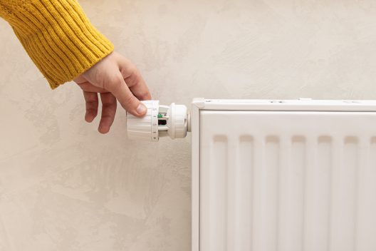 Mano ajustando el termostato de un radiador de calefacción para regular la temperatura y evitar el ambiente seco.