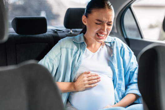 Mujer embarazada sintiendo dolor por contracciones en el asiento trasero de un coche de camino al hospital.