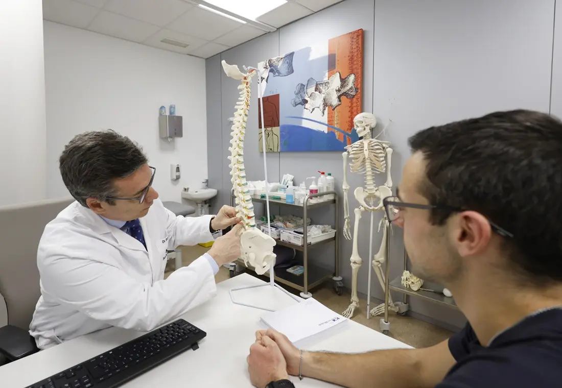 Traumatólogo con maqueta de columna vertebral explicando una patología en consulta